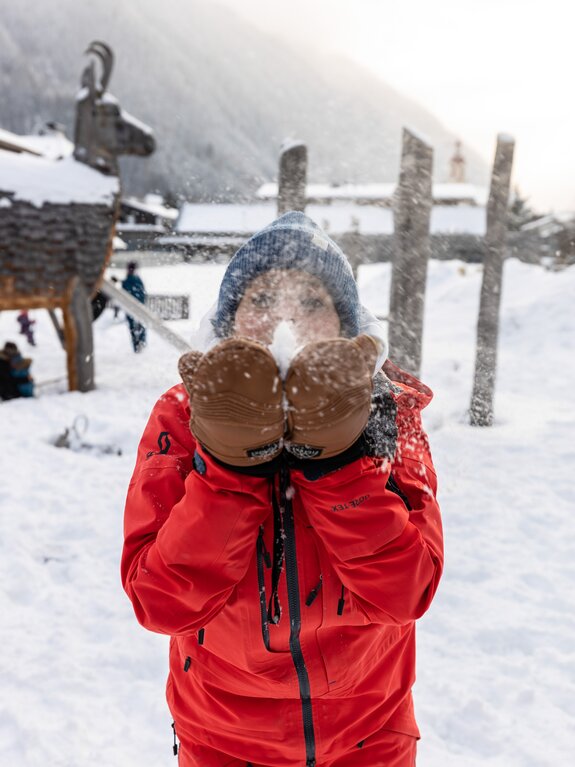 Kind mit Fäustlingen und roter Jacke pustet Schnee in die Luft