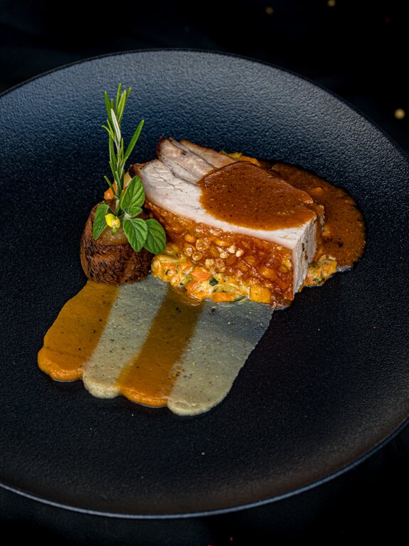 Schweinebraten mit Kruste auf Gemüse, Kartoffel und Soße auf dunklem Teller