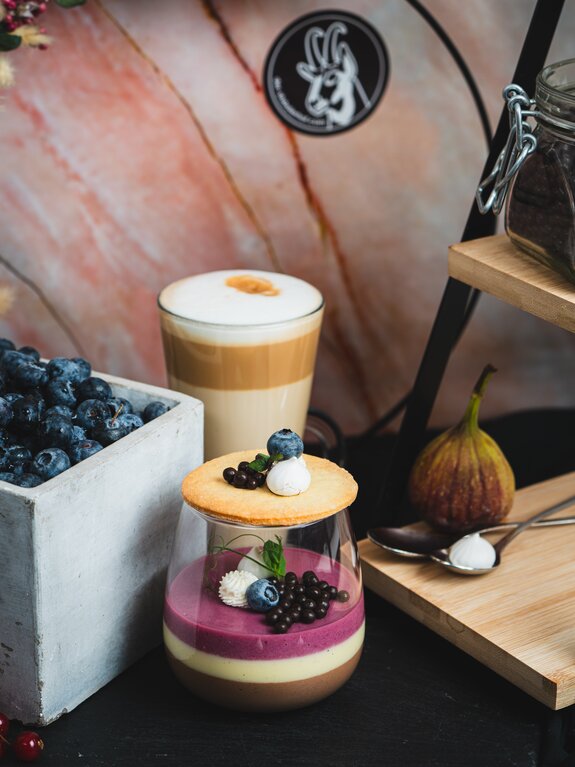 Dessert mit Blaubeeren, Feige und Latte Macchiato auf einem Tisch