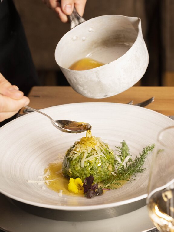 Koch beträufelt Spinatknödel mit Soße aus weißer Schale auf Teller