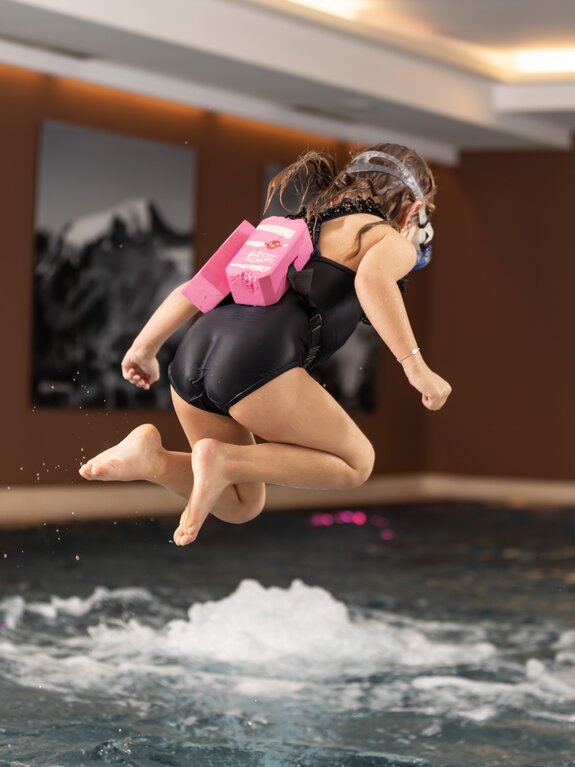 Mädchen springt mit Schwimmweste und Taucherbrille ins Schwimmbad