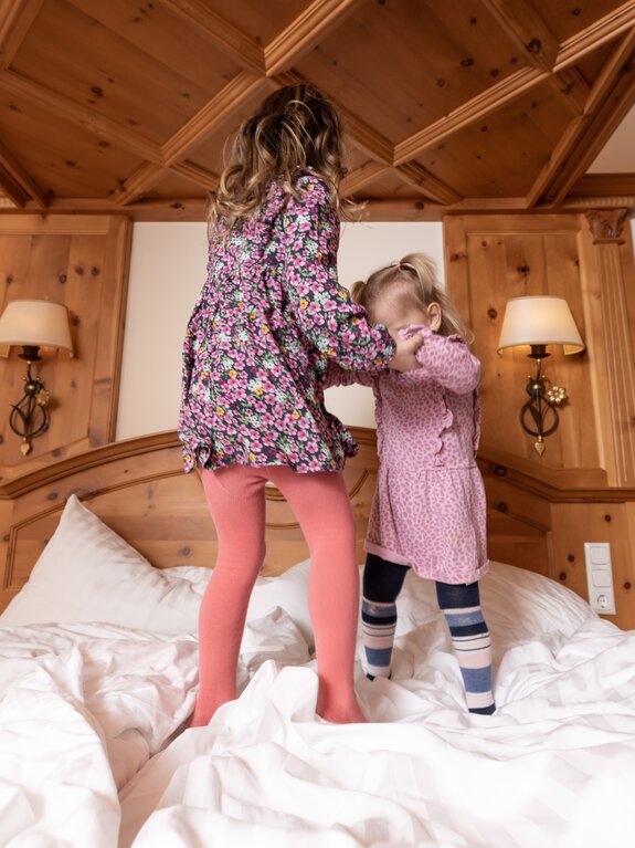 Zwei Mädchen springen auf einem Bett in einem Zimmer mit Holzvertäfelung