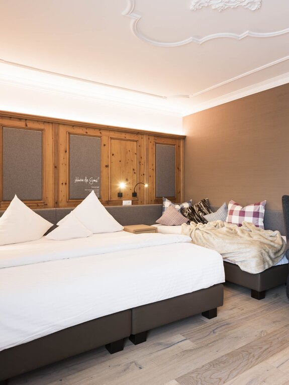Hotelzimmer mit Doppelbett, Couch und Sessel vor holzvertäfelter Wand
